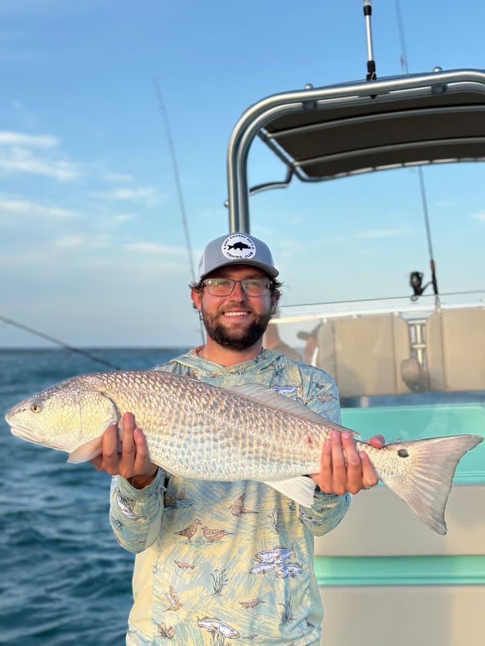 Angler holding a large redfish on a charter boat with the ocean horizon behind him at golden hour