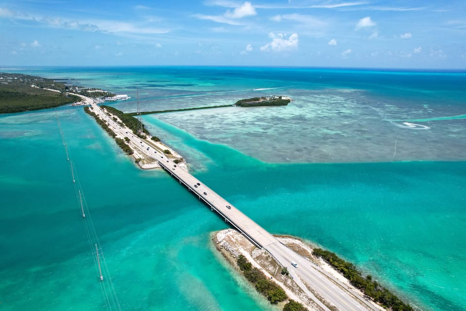 Aerial view of the Overseas Highway bridge stretching across turquoise Florida Keys waters between islands, with coral reef flats visible below